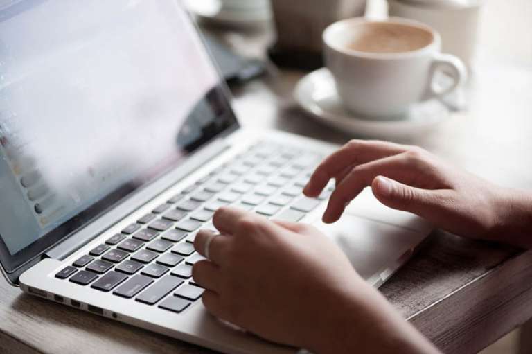 Young blonde woman freelancer typing in laptop in cafe